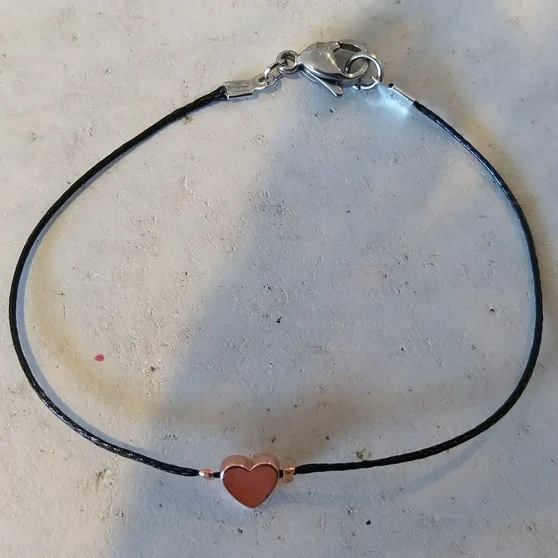 Bracelet sur cordon noir avec petit pendentif cœur doré-rose, porté au poignet