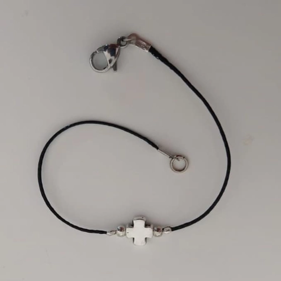 Bracelet sur cordon noir avec croix en métal argenté, porté au poignet
