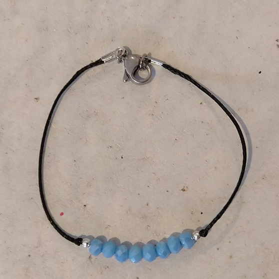 Bracelet sur cordon noir avec perle bleue nacrée, porté au poignet