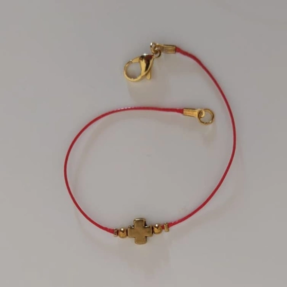 Bracelet sur cordon rouge à croix dorée, porté au poignet, lumière de fin d'après-midi